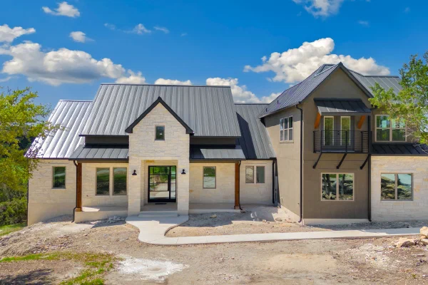 Front elevation blending white limestone, stucco, dark metal roofing, and a steel-railed second-story balcony