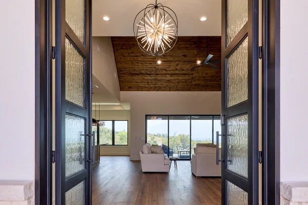 Steel and textured-glass entry doors framing views through the great room to a covered porch beyond