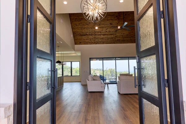 Iron-framed glass front doors opening to wood floors, an orb chandelier, and a stained tongue-and-groove ceiling