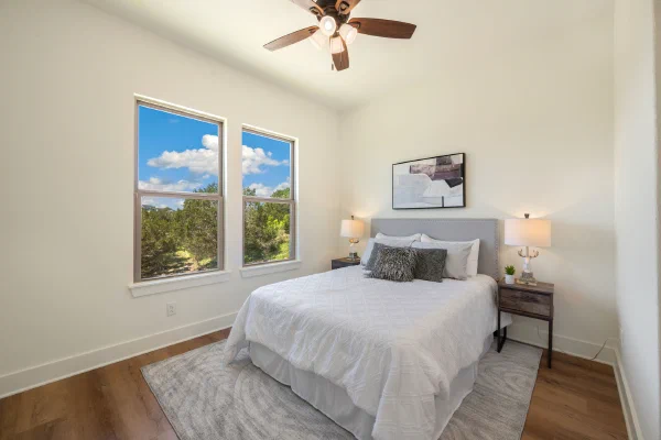 Guest bedroom with gray upholstered headboard and two tall windows framing wooded views