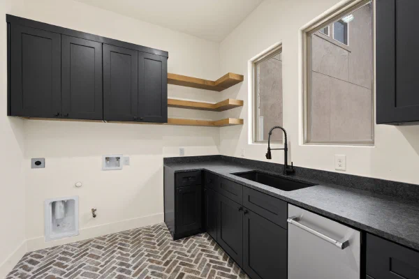Laundry room with black cabinetry, floating wood shelves, spring-coil faucet, and brick paver flooring