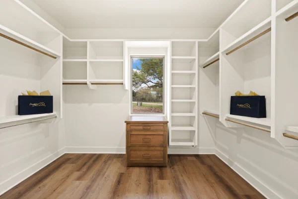 Walk-in closet with built-in shelving, hanging rods, and a knotty alder dresser beneath a picture window
