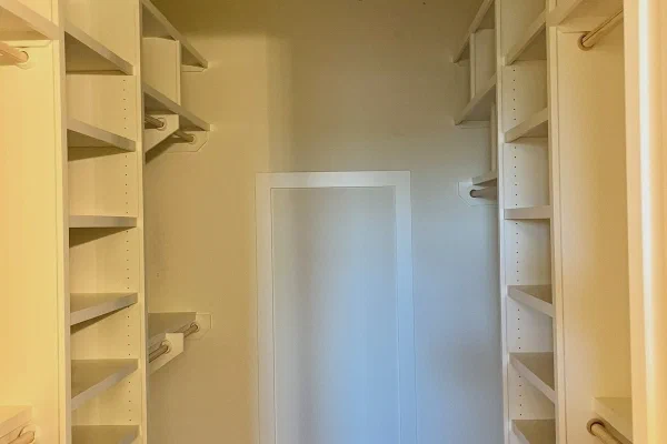 Walk-in closet with floor-to-ceiling white shelving, double hanging rods, and dark wood flooring