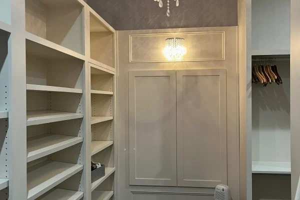 Boutique-style walk-in closet with crystal drum chandelier, shoe shelves, and paneled built-in wardrobe