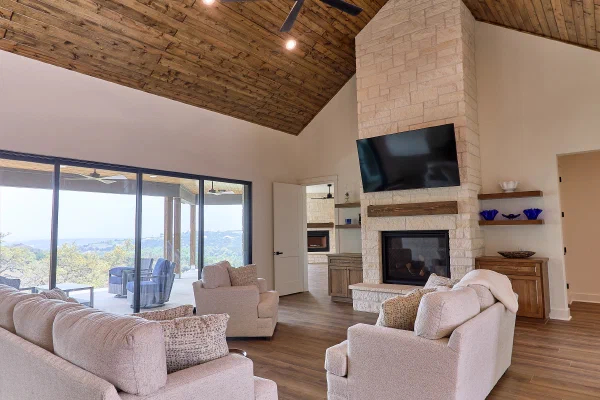 Cathedral wood plank ceiling and towering stone fireplace anchoring the living room of a custom home