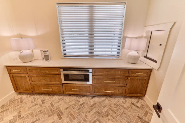 Full wall of oak Shaker cabinets with brass hardware and built-in microwave drawer under a wide window