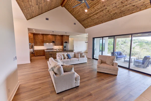 Great room under a vaulted knotty pine ceiling with oak kitchen cabinetry and glass sliders to a covered patio