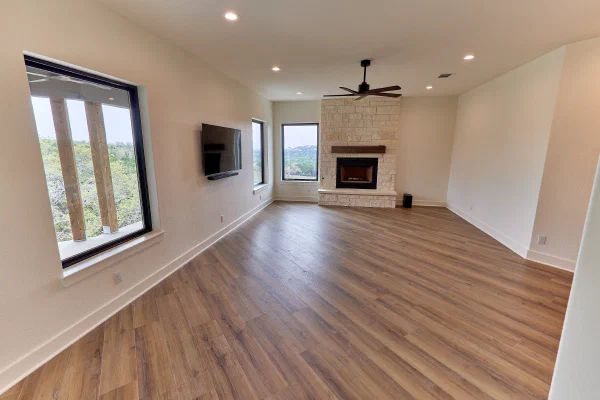 Austin stone corner fireplace with cedar mantel anchors a bright bonus room with wood-look plank flooring