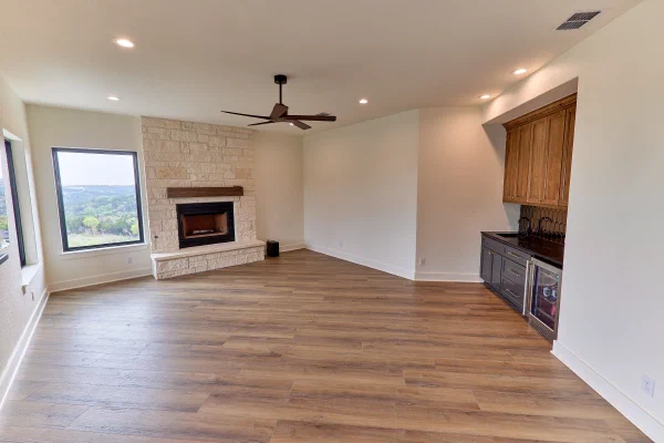 Bonus room with limestone fireplace, timber mantel, and wet bar nook with beverage cooler and dark counters