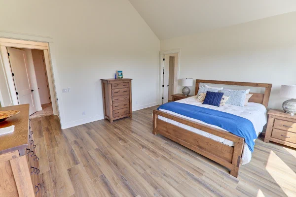 Custom home primary bedroom with oak chest, king bed in blue and white linens, and wide plank floors