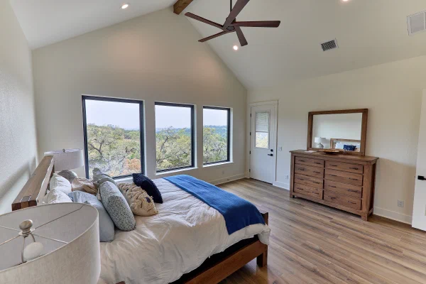 Vaulted primary bedroom with walnut ceiling fan, exterior patio door, and eight-drawer oak dresser with mirror