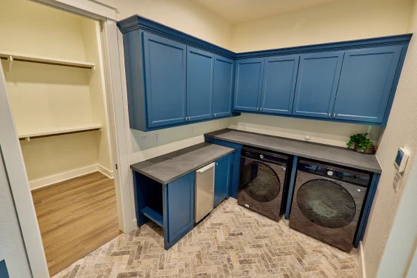 Deep blue laundry cabinets with folding counter over front-load washer and dryer, plus under-counter ice maker