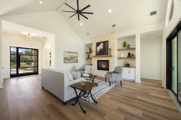 Living room with white stone fireplace, floating oak shelves, built-in cabinets, and a black iron glass front door