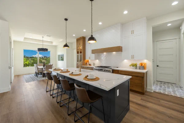 Black island with quartz top and leather stools under bronze pendants, white cabinets and wood-trimmed shiplap hood