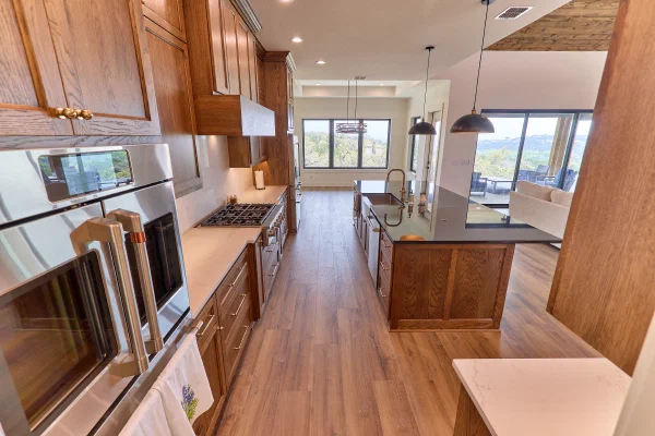 Stainless wall ovens and gas cooktop line oak cabinetry across from a black granite island with farmhouse sink