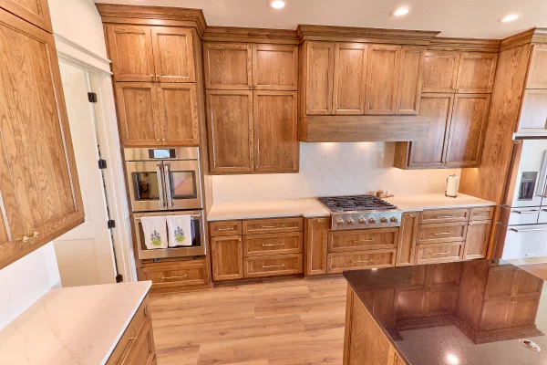 Crown-molded oak cabinets with wood vent hood, veined quartz backsplash and stainless cooktop beside a granite island