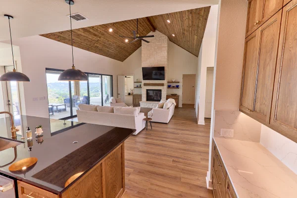 Black granite counters and oak cabinets open to a vaulted living room with stone fireplace and sliding glass doors