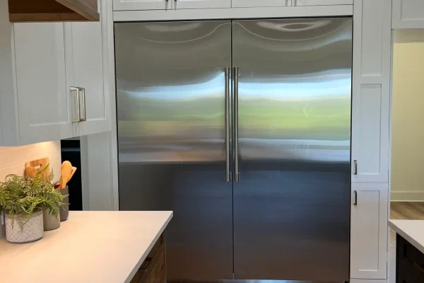 Full-height stainless refrigerator and freezer columns framed by white shaker cabinets and wood island drawers