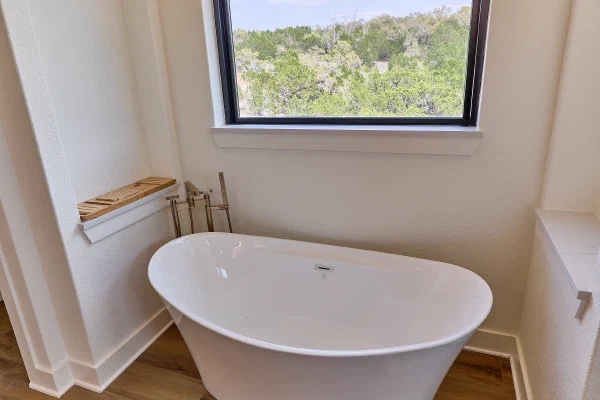 Oval soaking tub framed by a Texas Hill Country window view, dandelion crystal chandelier, and brass tub filler