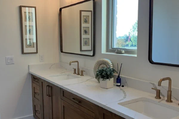 Custom home double vanity with veined quartz top, brass widespread faucets, and bronze-framed mirrors